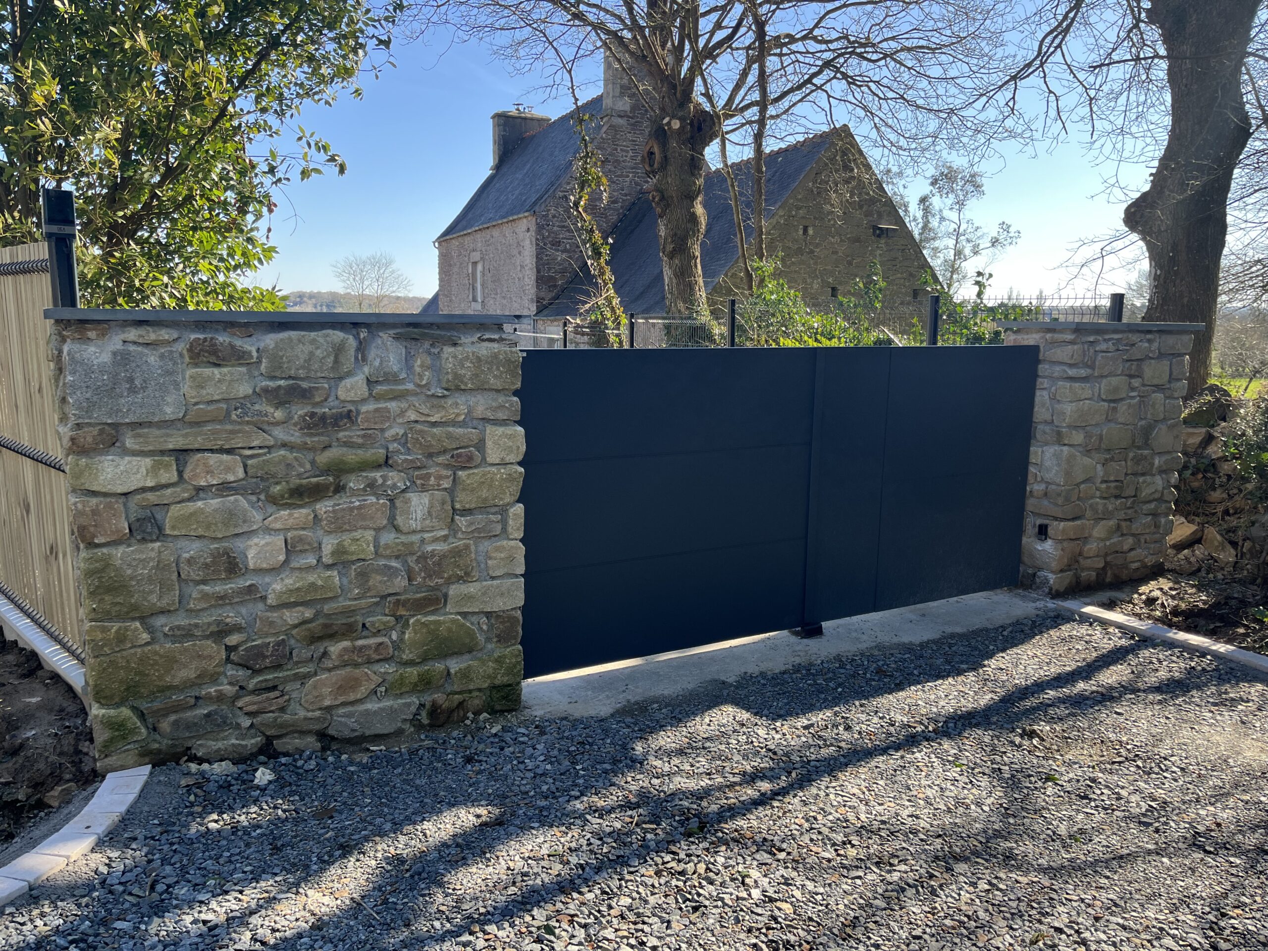Portail neuf automatisé installé entre deux piliers en pierre